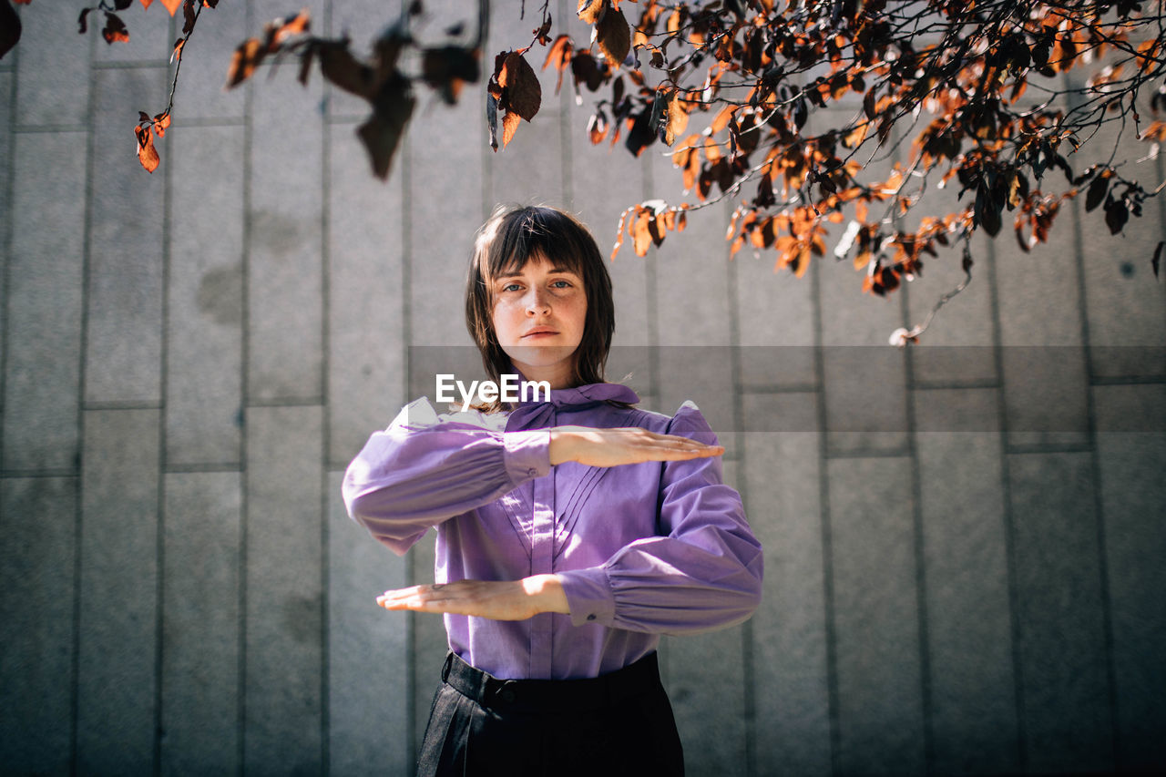 PORTRAIT OF SMILING WOMAN STANDING AGAINST WALL