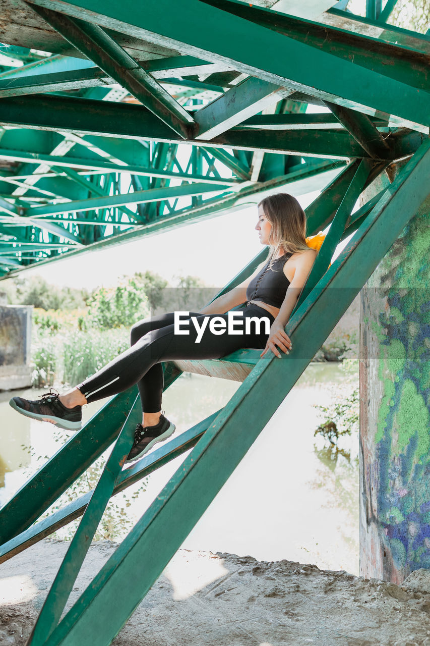 Full length of young woman sitting on railway bridge