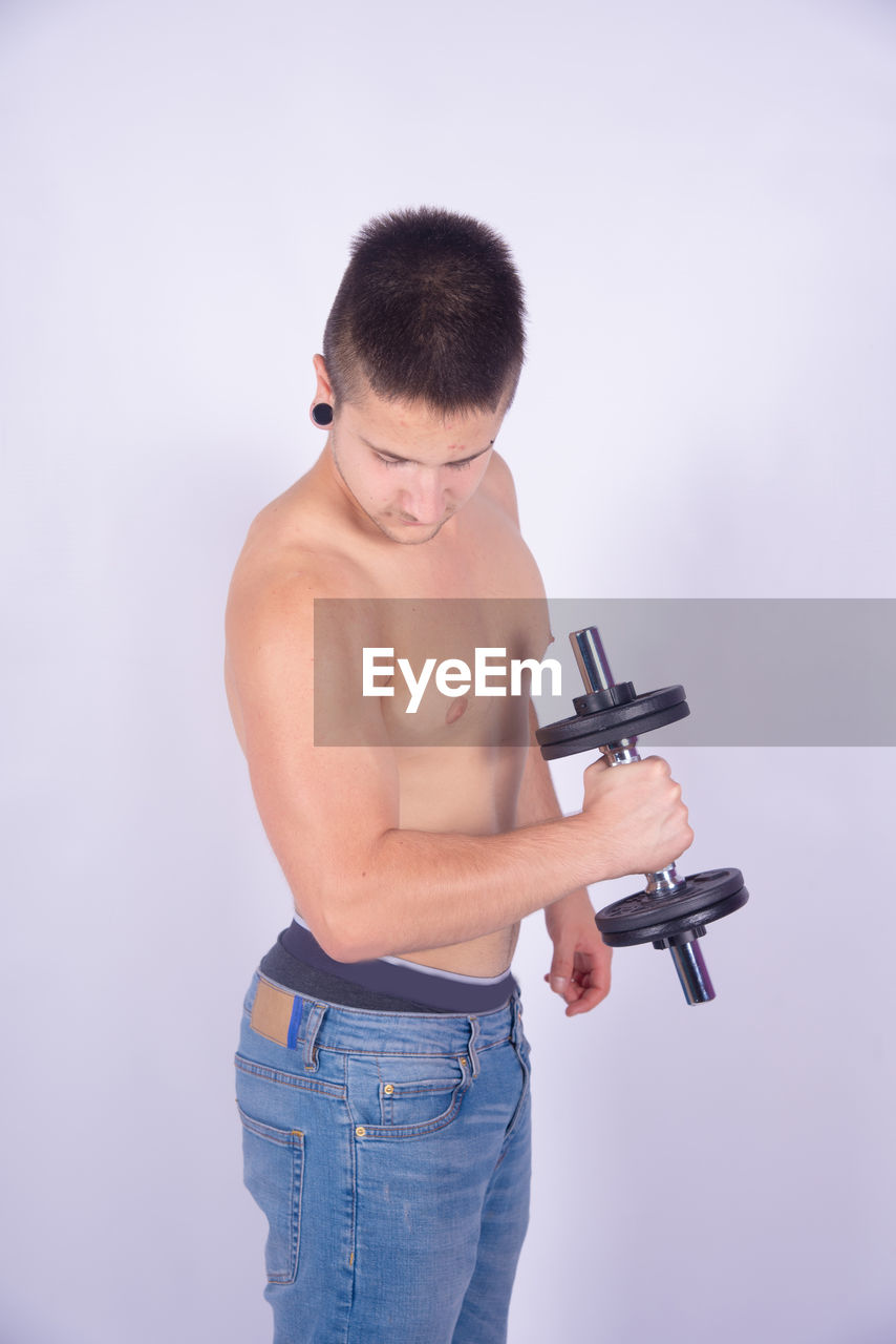 Shirtless man lifting dumbbells against purple background