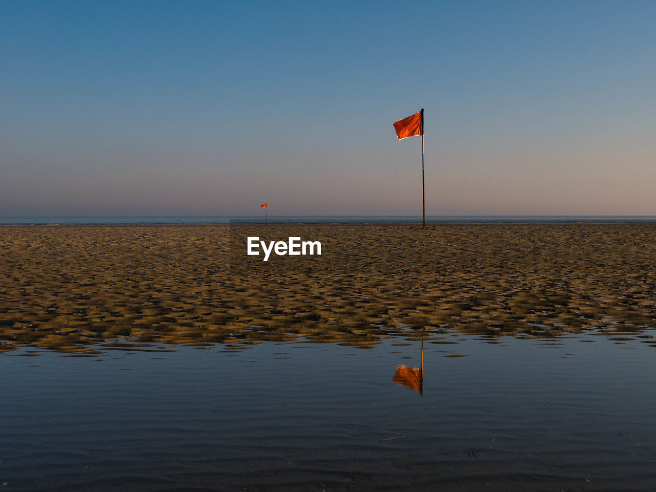 Red flag mirroring in water during morning hours at a beach in northern france