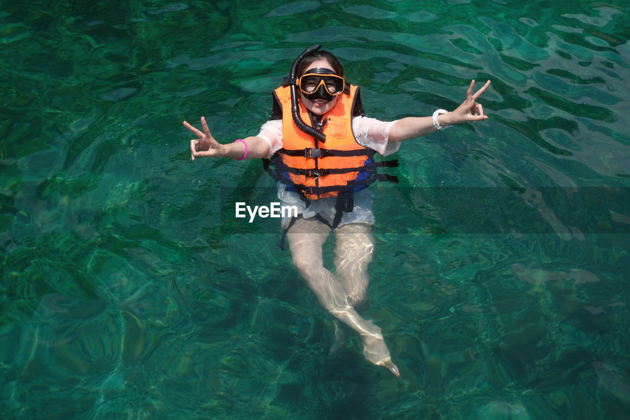 Portrait of smiling young woman showing peace sign while swimming in sea