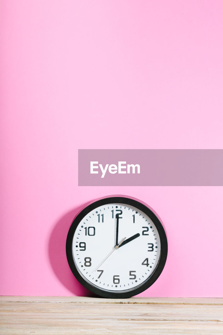Close-up of clock on wooden table against pink wall