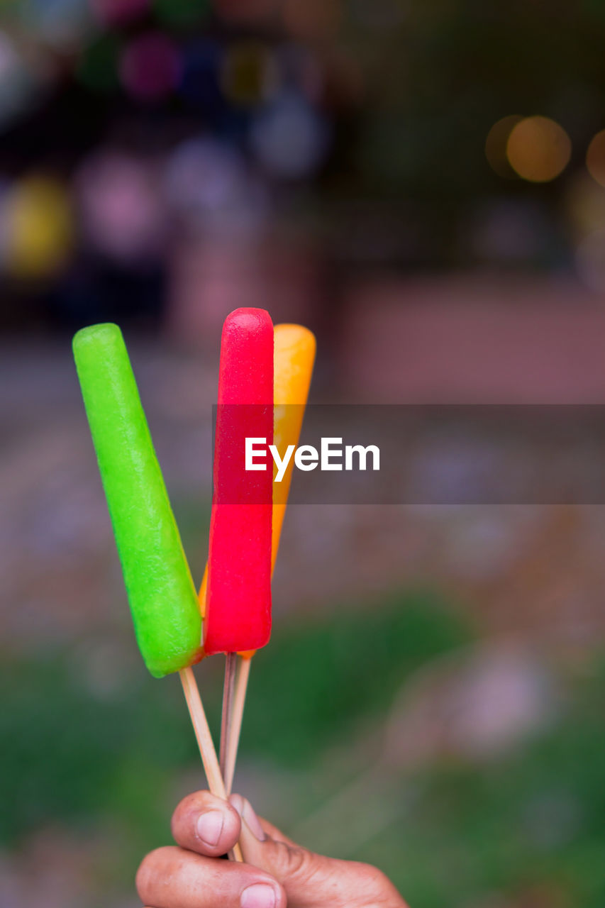 Close-up of hand holding colorful flavored ice outdoors