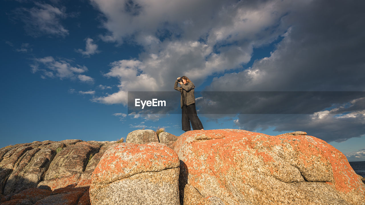 Low angle view of young woman standing on rock against sky