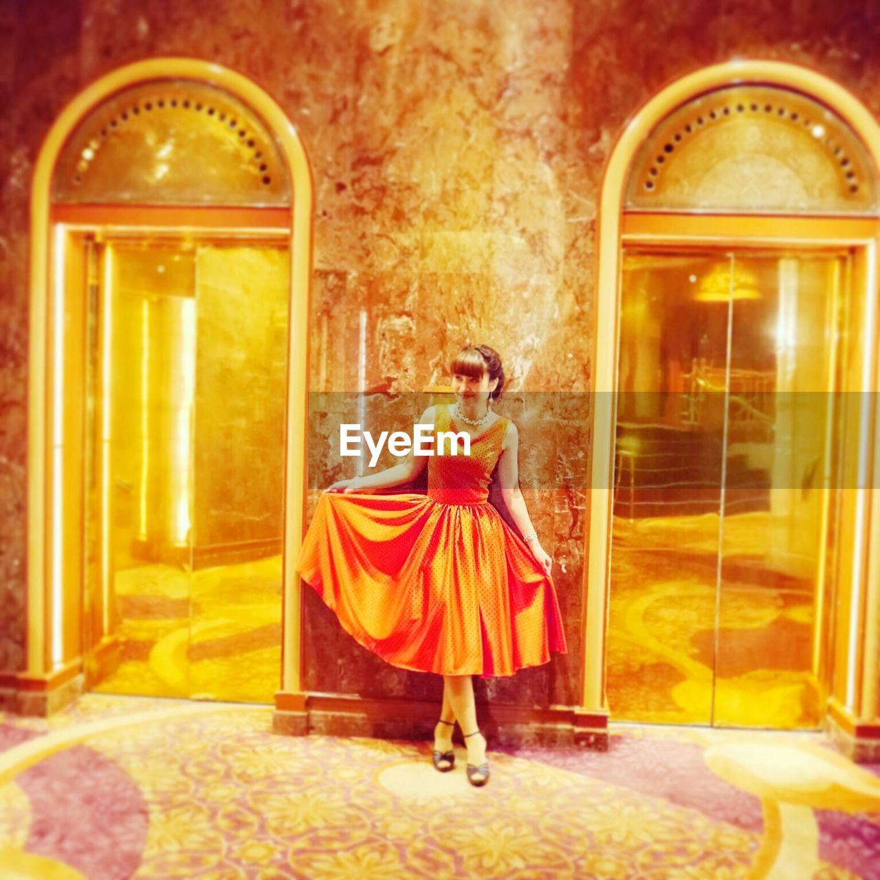 Full length of smiling woman posing by illuminated elevators