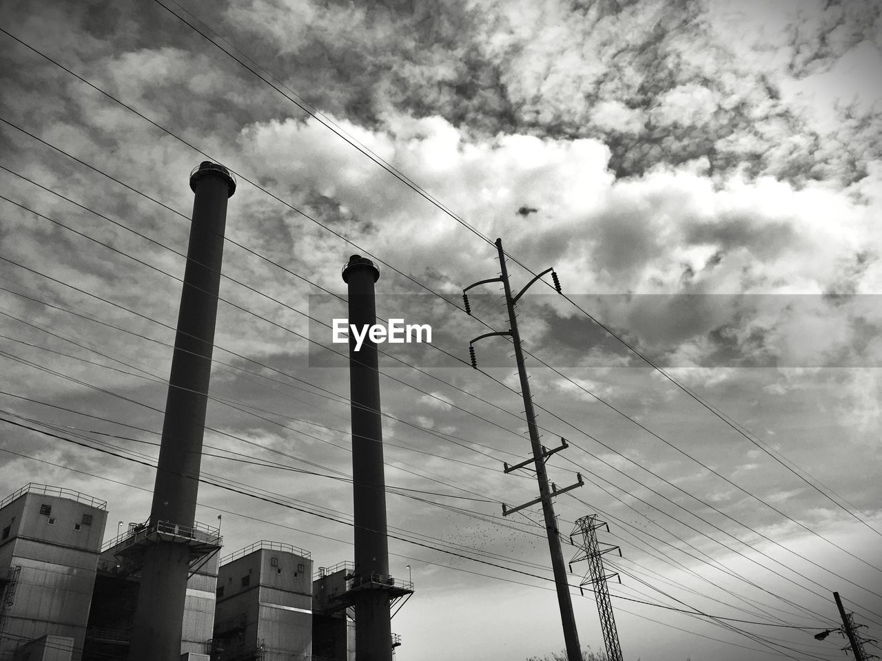 Low angle view of electricity pylons and smoke stacks