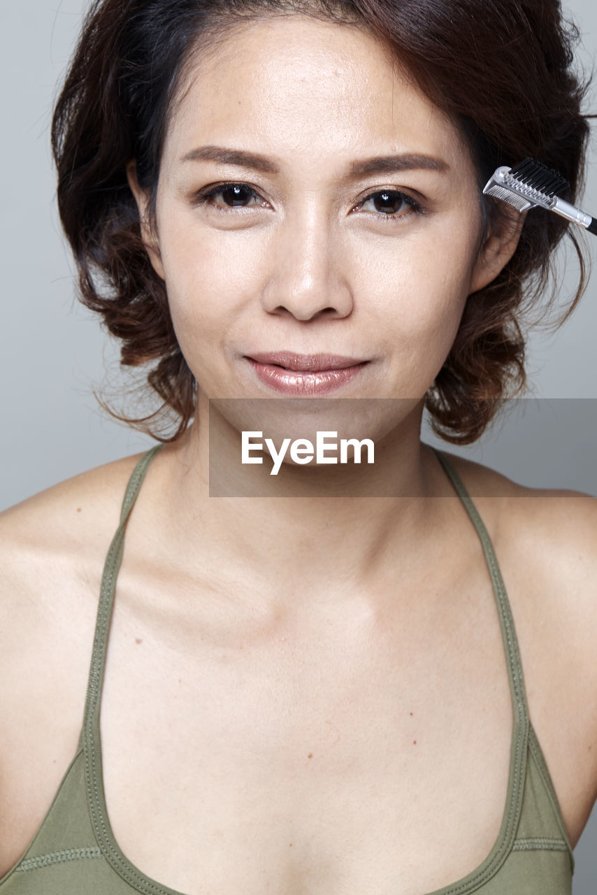 Portrait of smiling beautiful woman holding mascara applicator against gray background