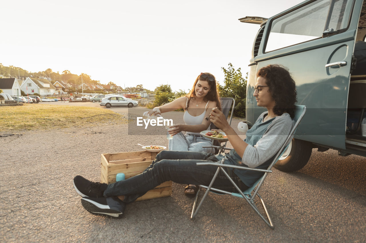 Young couple having food outside camping van in evening
