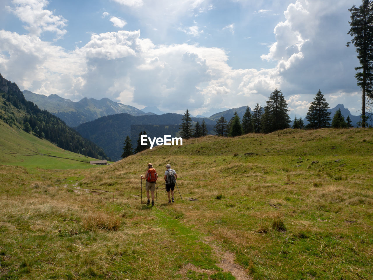 REAR VIEW OF MEN WALKING ON STREET AMIDST MOUNTAINS AGAINST SKY