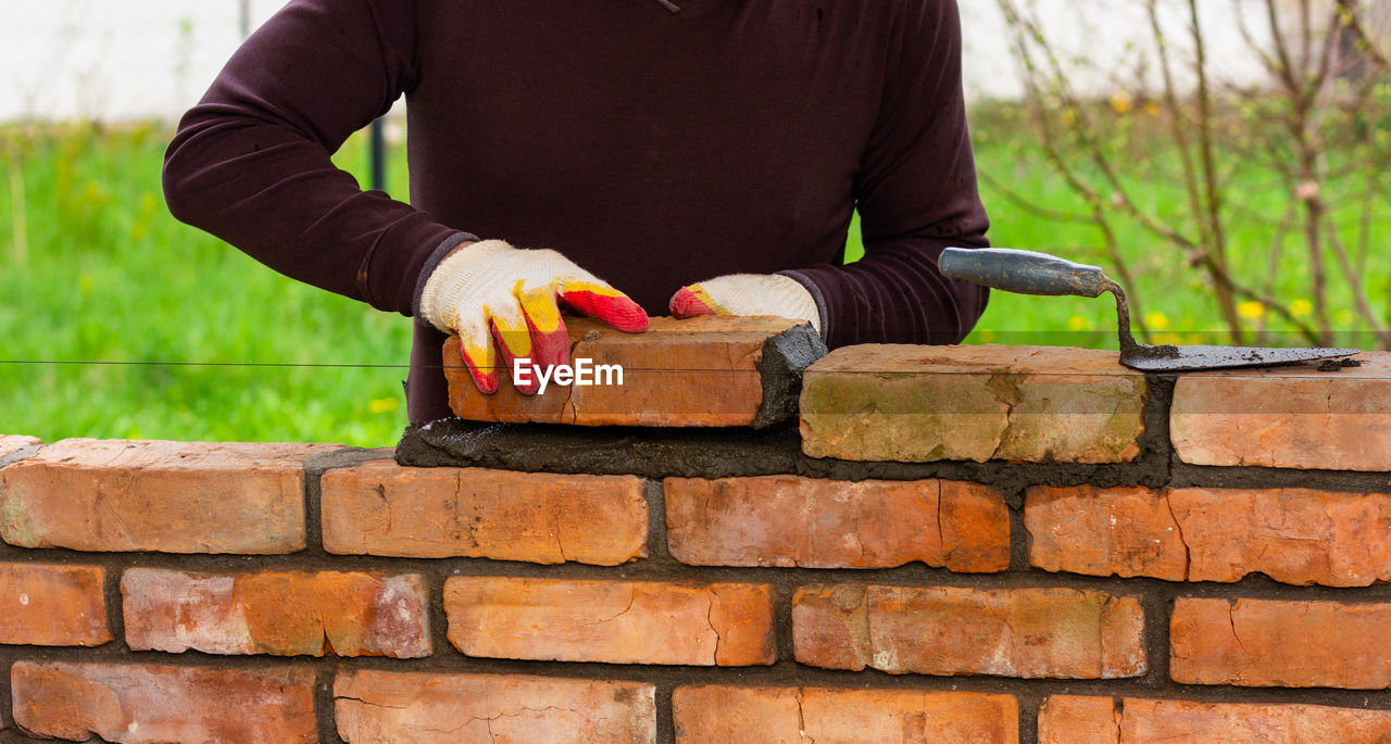 A man builds a wall of bricks, lays a brick on a cement-sand mortar