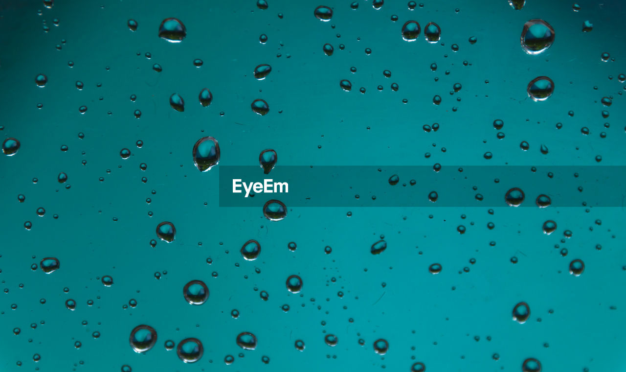 Full frame shot of water drops on glass against blue sky