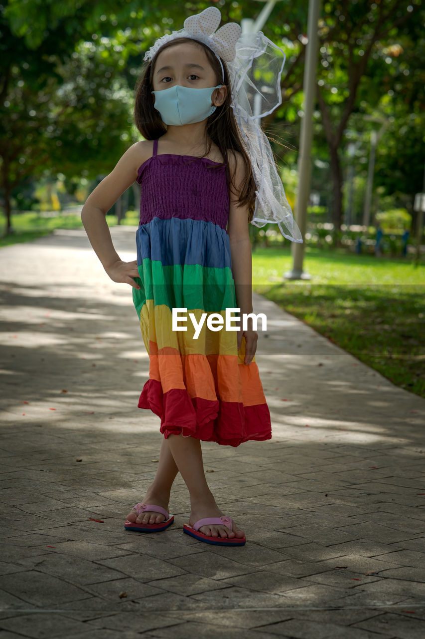 Little girl wearing face mask with rainbow dress enjoying outdoor in the park. new normal.