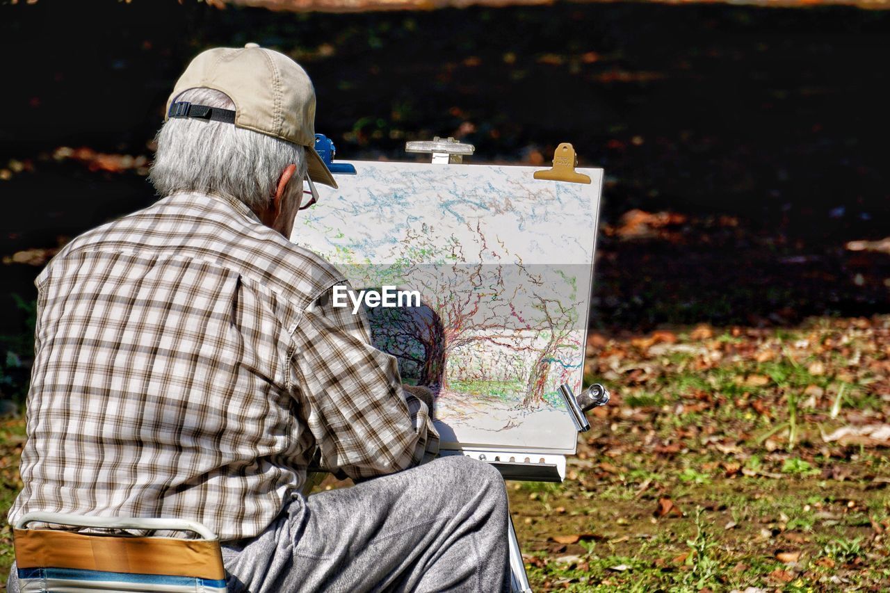 Rear view of senior man painting on canvas on field