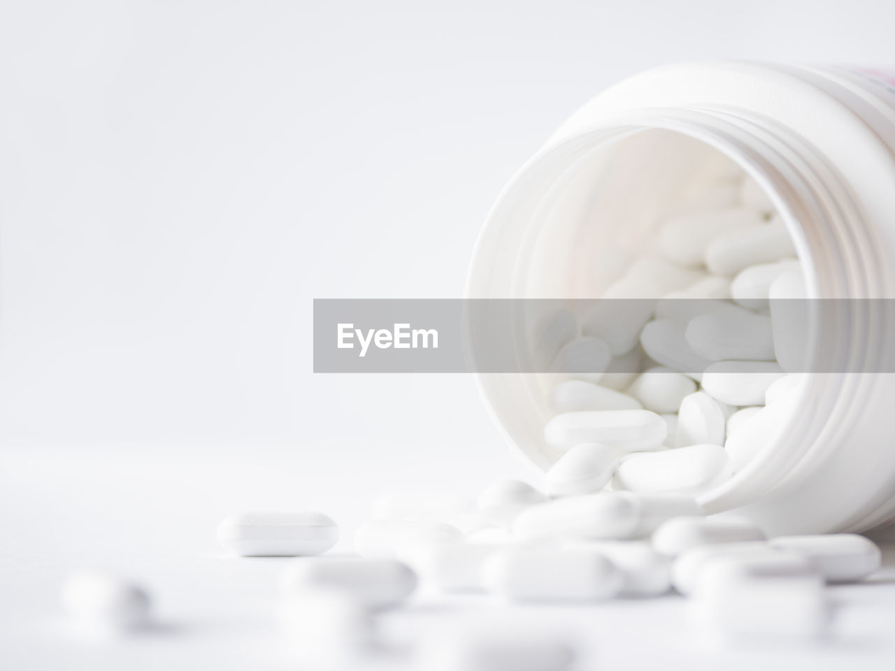 White pills spilled out of a plastic jar. medicine capsules on white background with copy space.