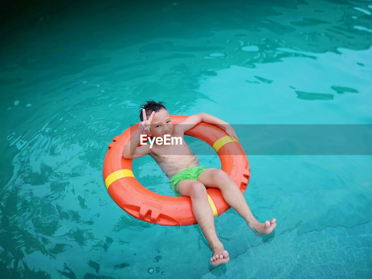 High angle view of shirtless boy sitting on inflatable ring in pool