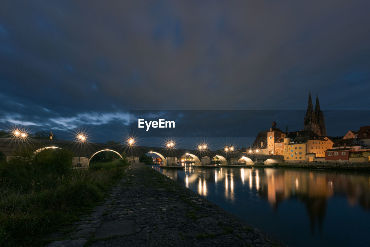 RIVER AMIDST ILLUMINATED CITY BUILDINGS AGAINST SKY AT DUSK