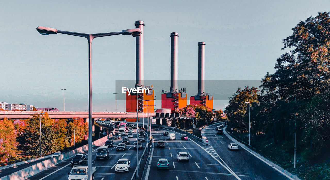 Traffic on road and factory chimneys in city against sky