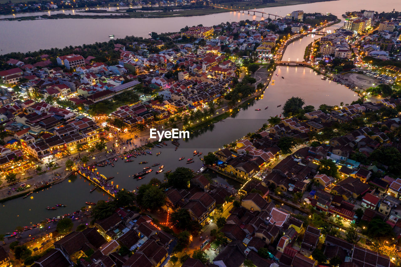 High angle view of illuminated buildings by river against sky