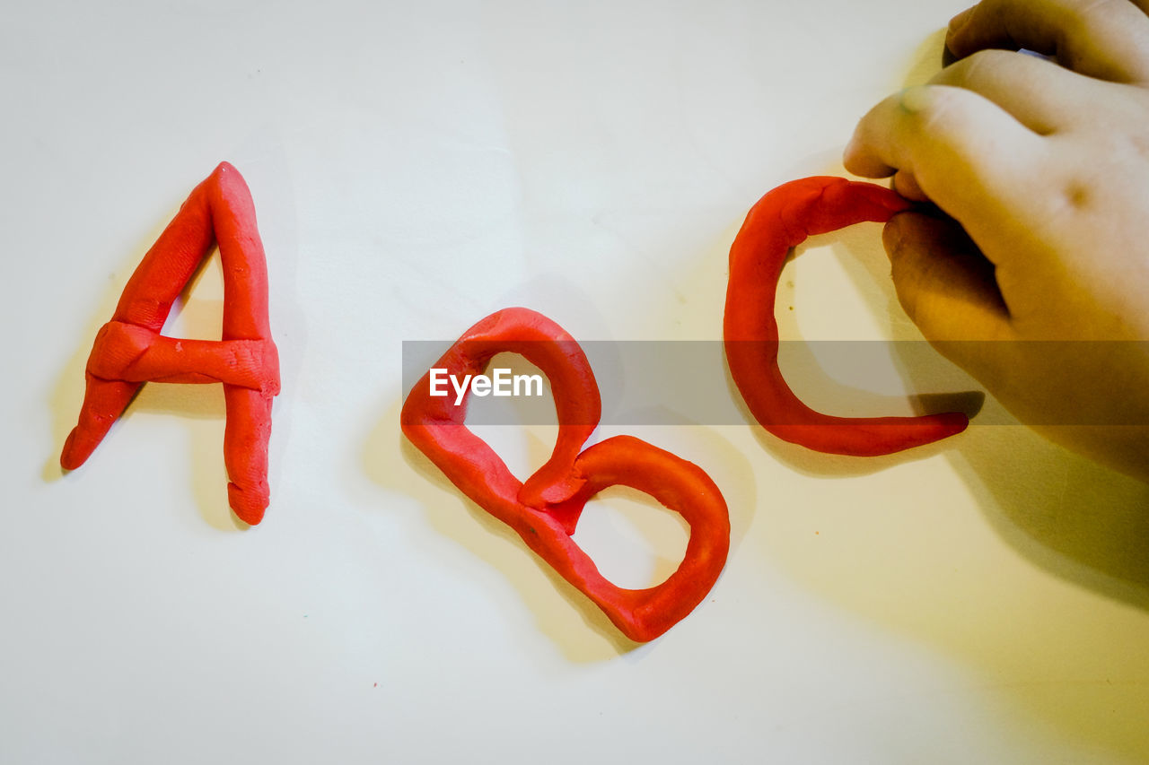 Cropped hand making alphabets with modelling clay on white table