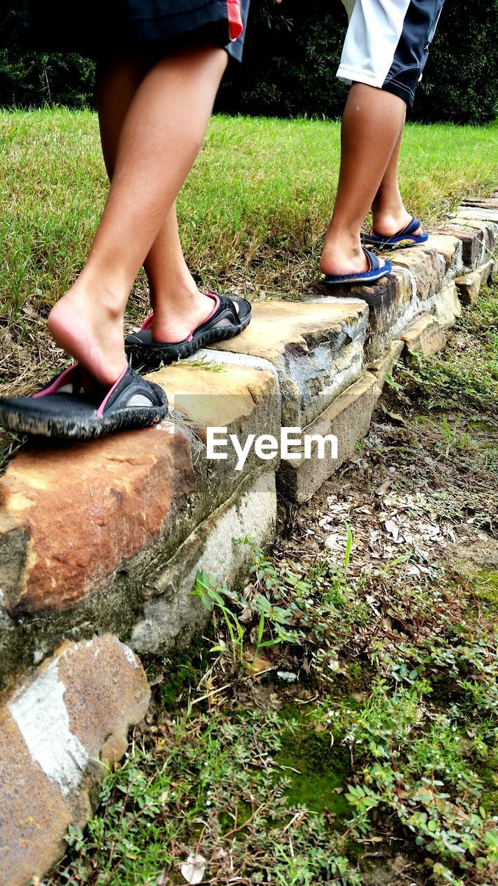 Low section of boys walking on retaining wall by grass