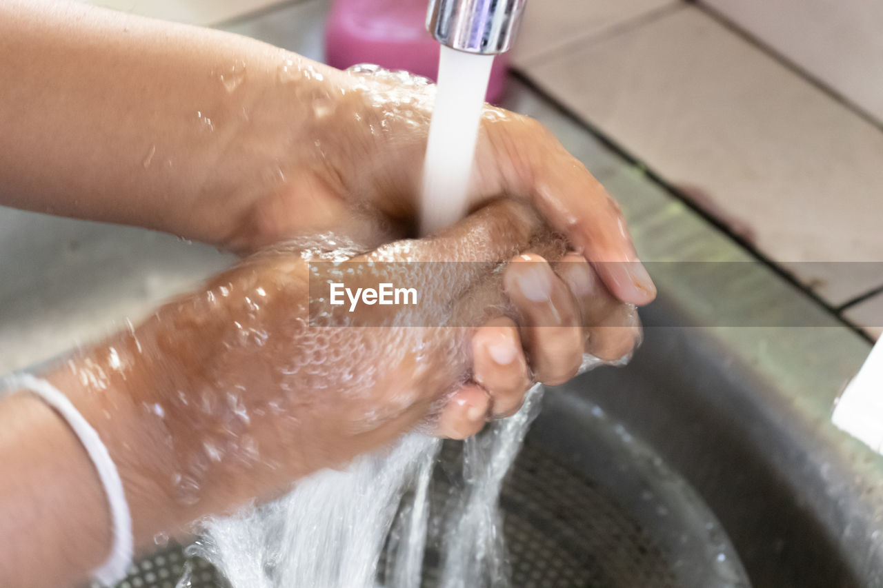 CROPPED IMAGE OF HAND TOUCHING WATER AT BATHROOM