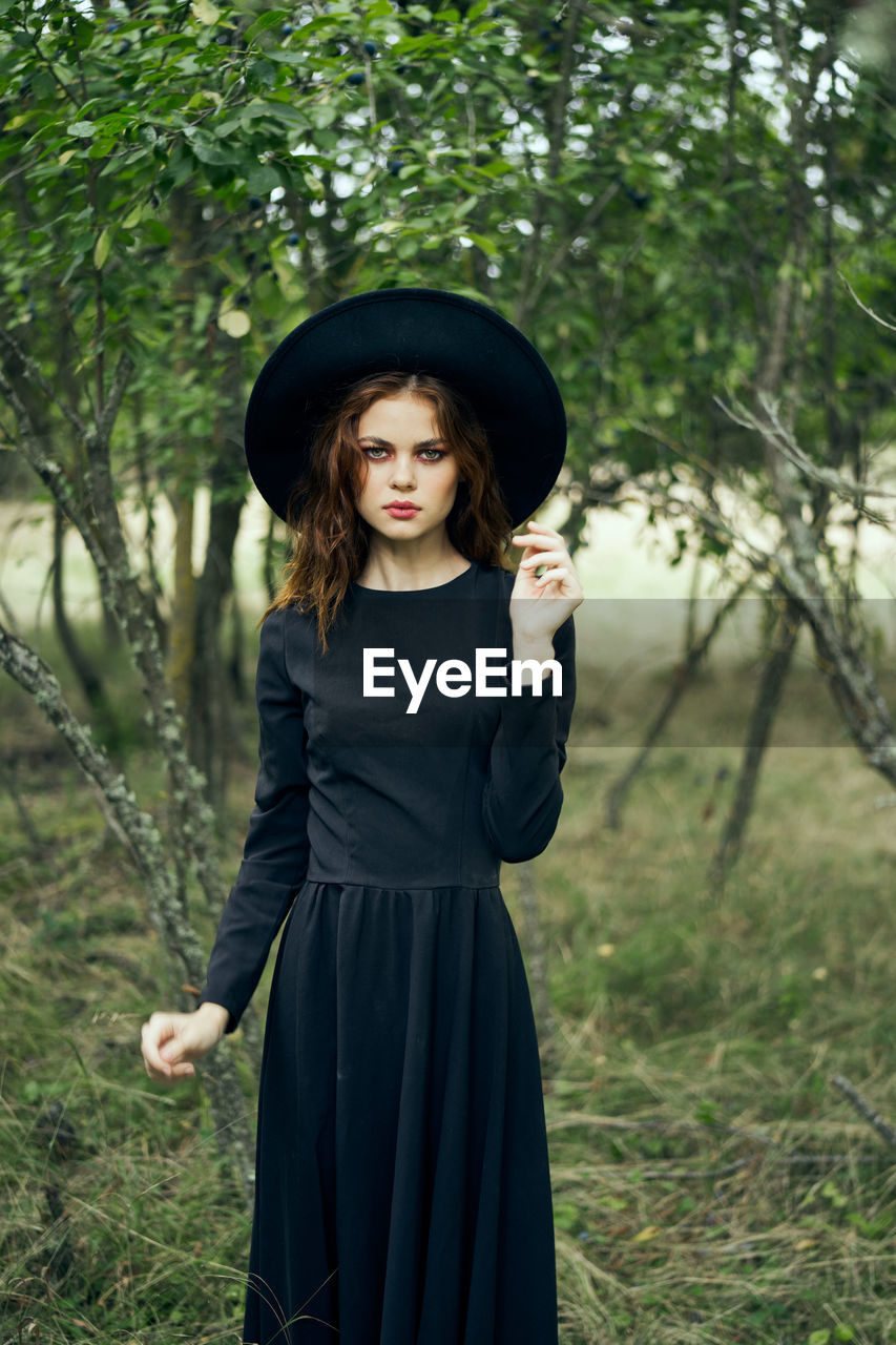 portrait of young woman standing against trees