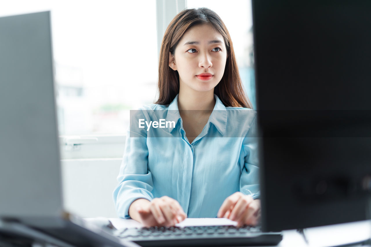 portrait of young woman using mobile phone while sitting in office