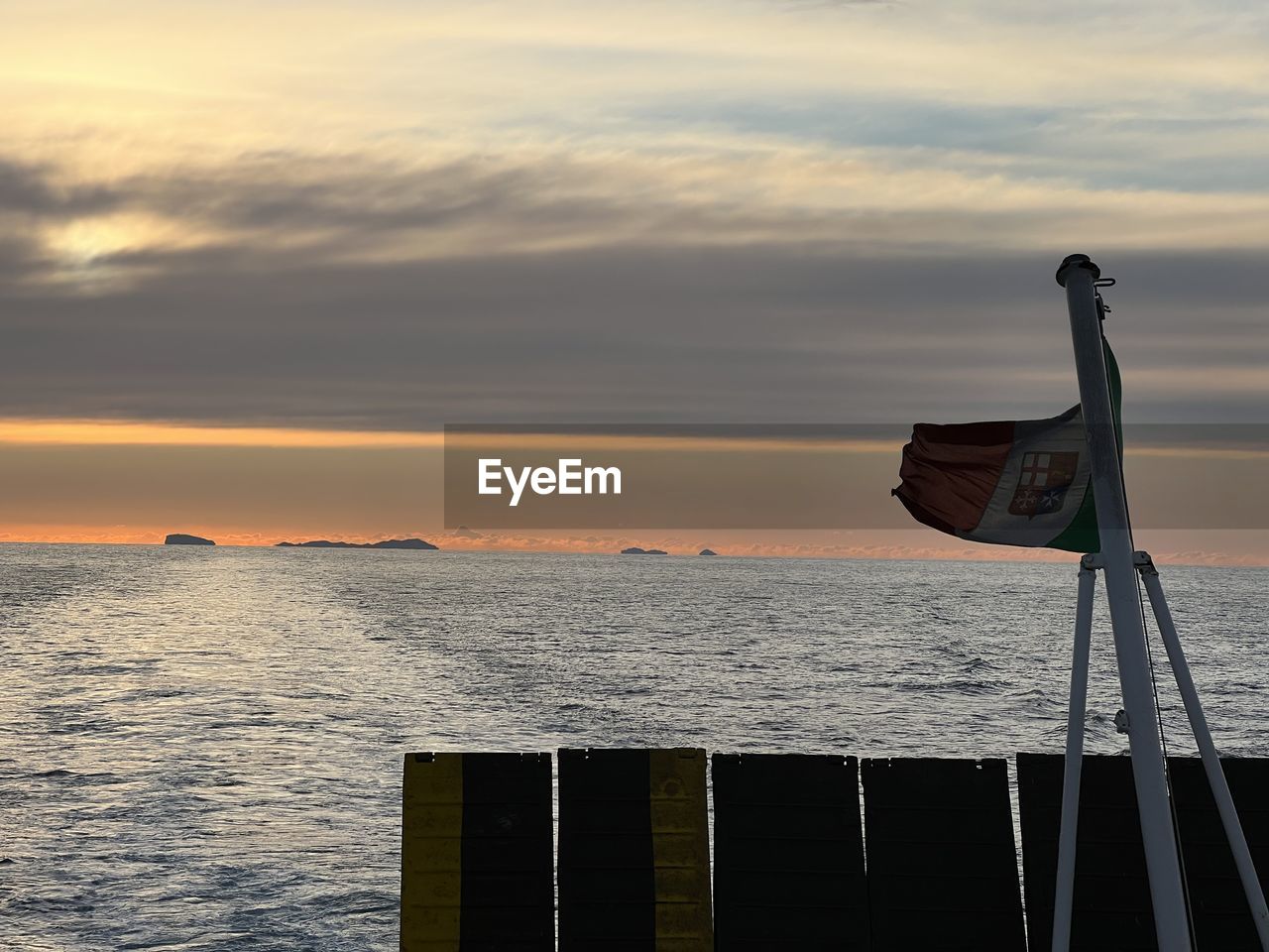 sky, water, sea, ocean, sunset, horizon, nature, cloud, coast, beauty in nature, evening, dusk, reflection, scenics - nature, no people, tranquility, horizon over water, transportation, flag, vehicle, nautical vessel, tranquil scene, outdoors, shore, wave, travel, environment, ship, sunlight, mode of transportation, land, architecture, beach, sun, idyllic