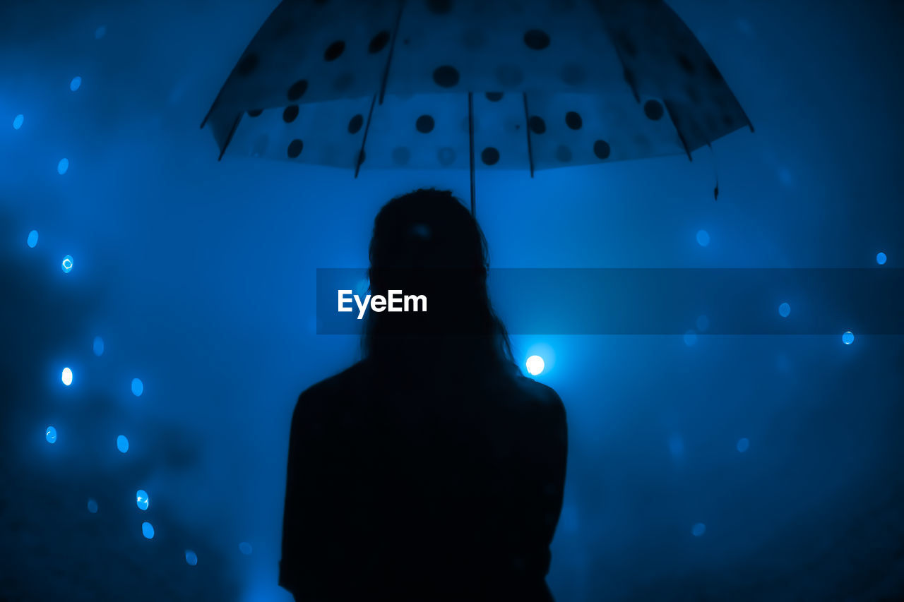 Woman holding umbrella while standing against illuminated lights at night