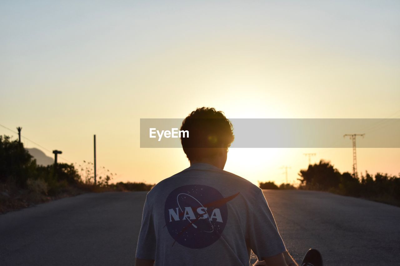 REAR VIEW OF MAN STANDING ON ROAD AGAINST SKY