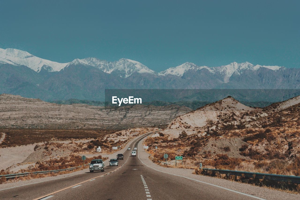 Road leading towards mountains against clear sky