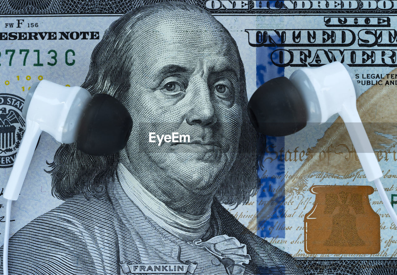 In this photo illustration earphones near franklin's ears on a 100 dollar bill