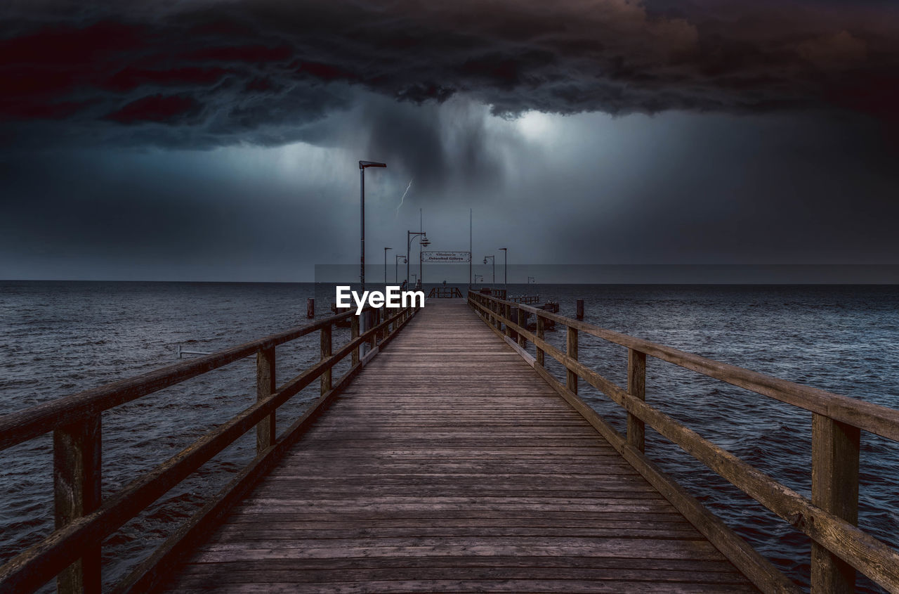 Pier over sea against storm clouds