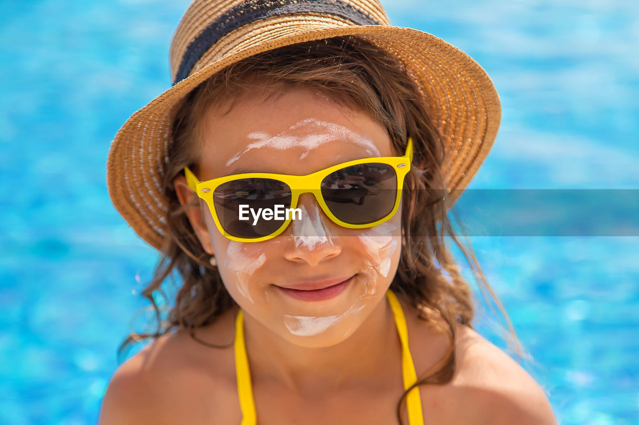 Portrait of girl wearing suntan lotion against swimming pool