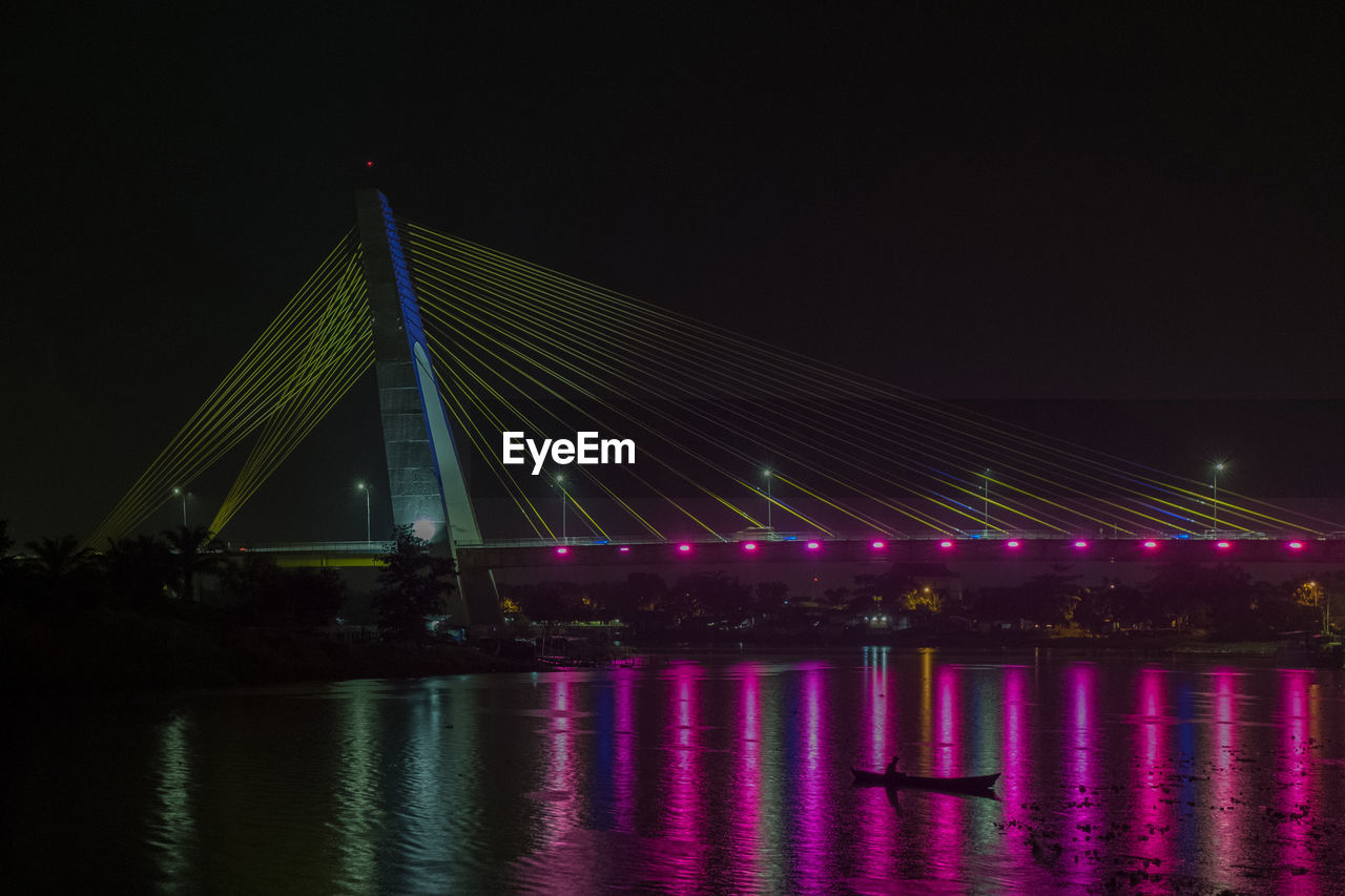 Illuminated bridge over river against sky at night