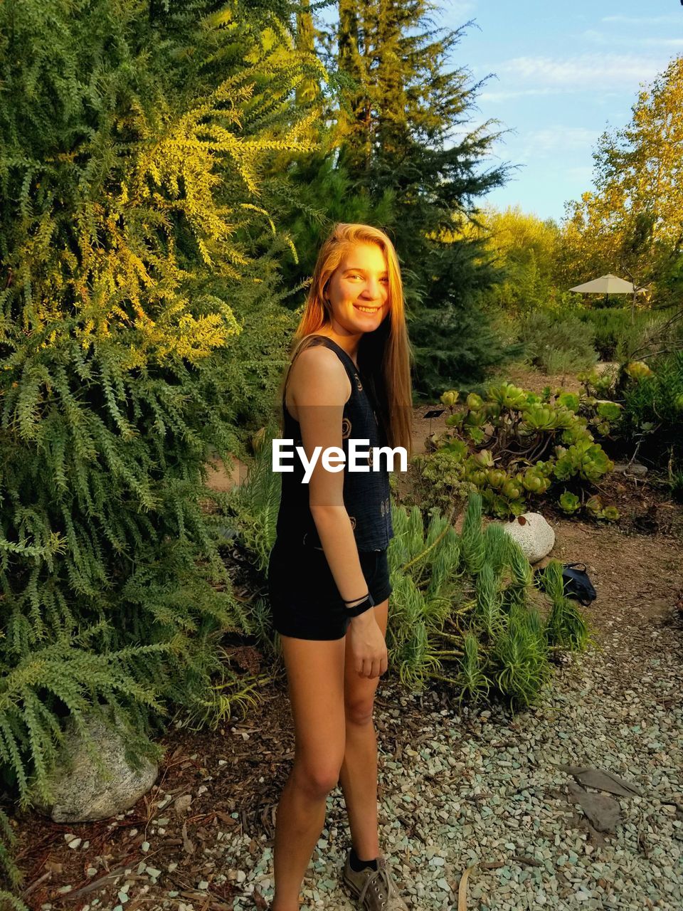 Portrait of smiling young woman standing against plants