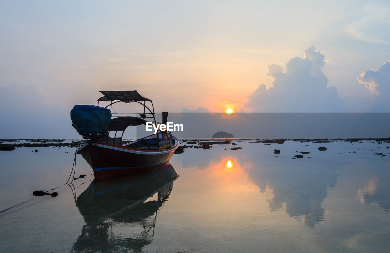 Fishing boat moored in sea against sky during sunset