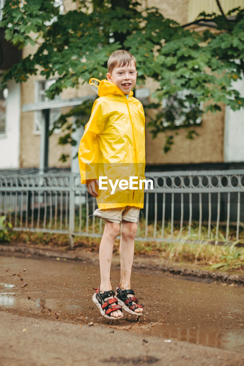 A boy in a yellow raincoat walks outside in the rain. a child jumps on the narrows. 