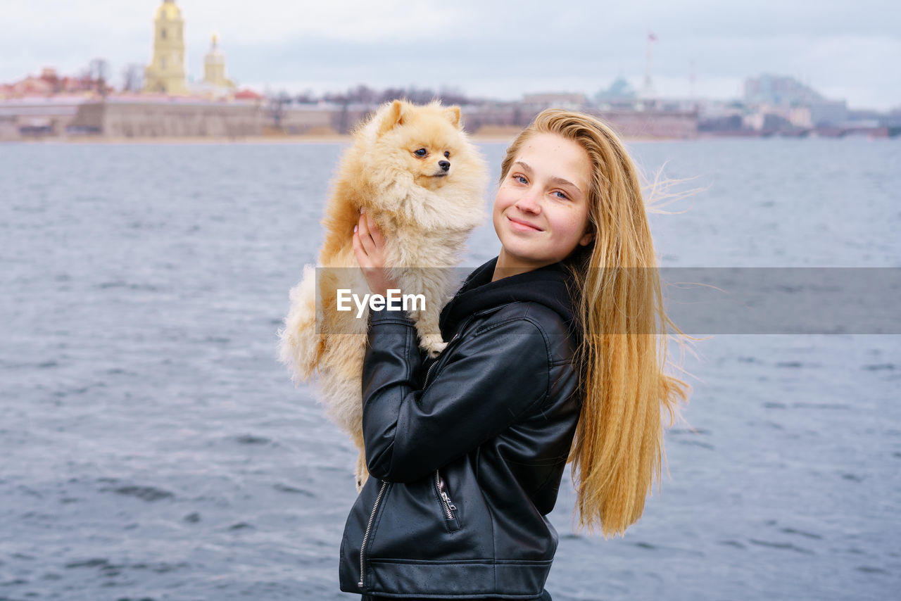 Young woman hugs spitz dog outdoors on embankment of city river in black