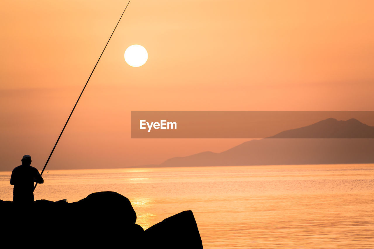 Silhouette man fishing by sea against sky during sunset