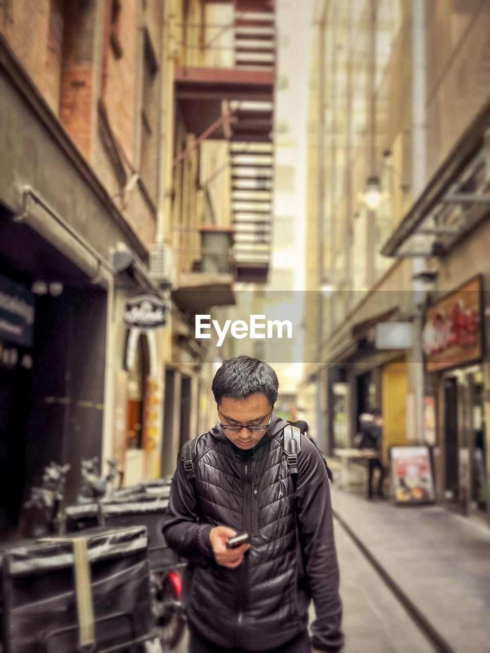 Portrait of young man using smartphone in alley against buildings in the city.