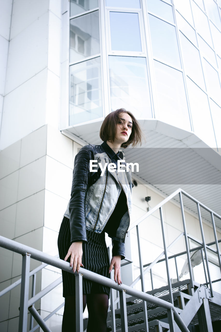 Portrait of young woman leaning on railing against building