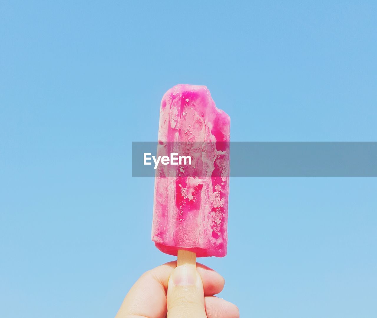 Cropped image of person holding popsicle against blue background