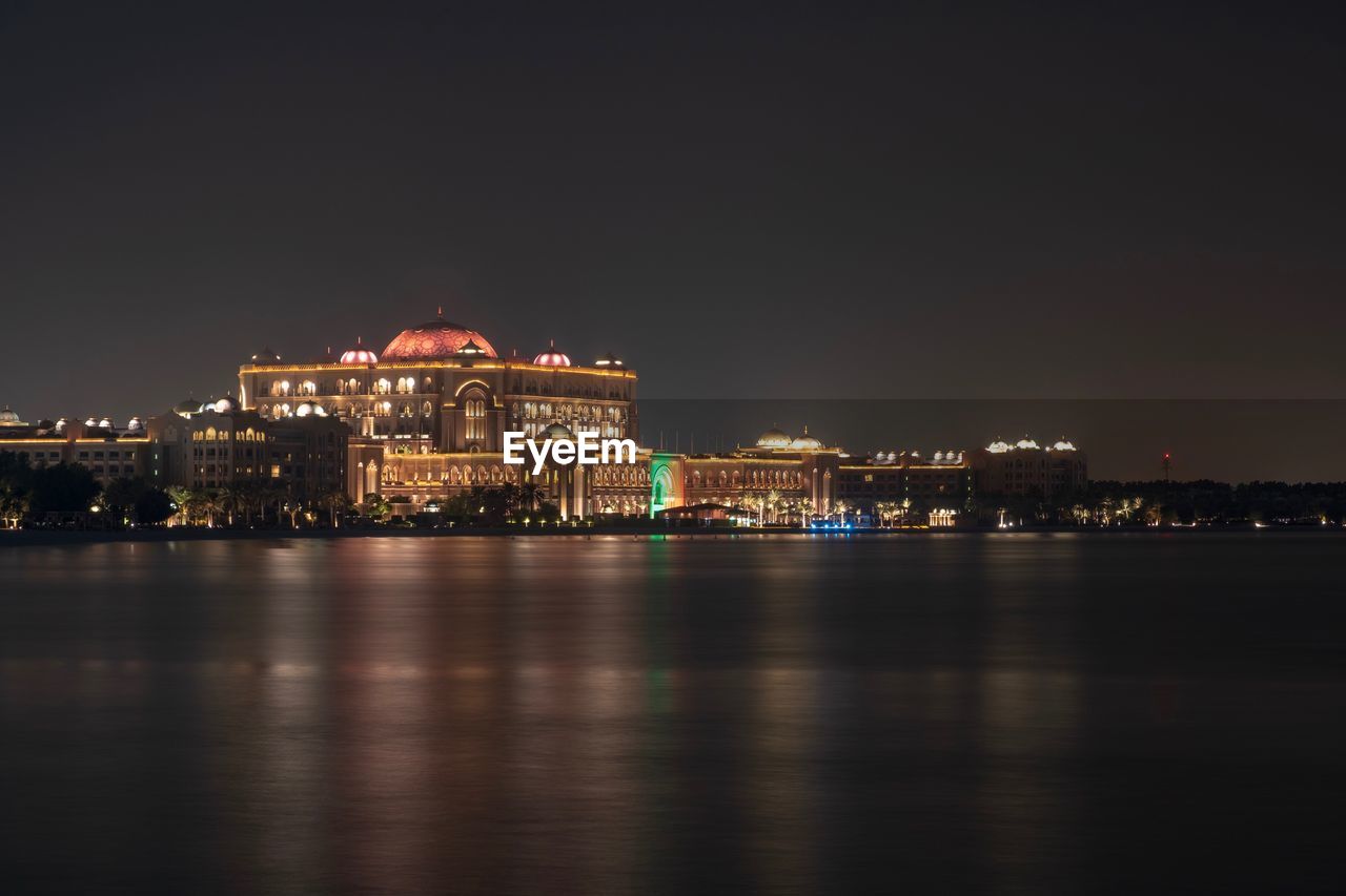 ILLUMINATED BUILDINGS BY RIVER AGAINST SKY