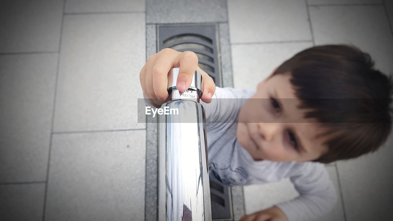 High angle view of boy holding faucet