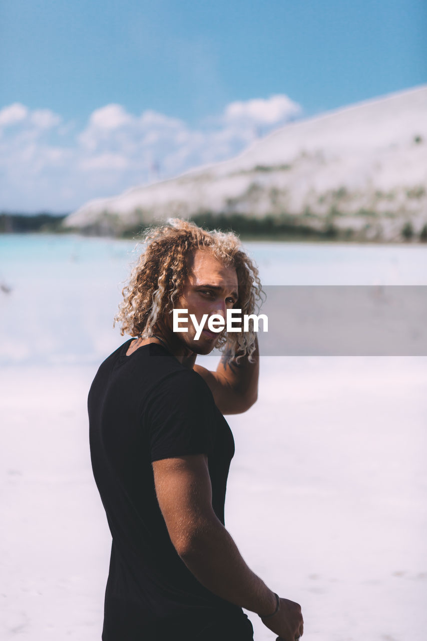 Portrait of man with curly hair standing at beach