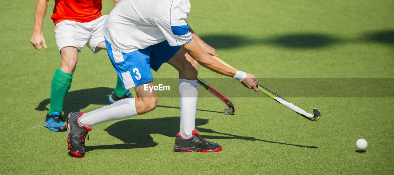 Low section of men playing hockey on turf