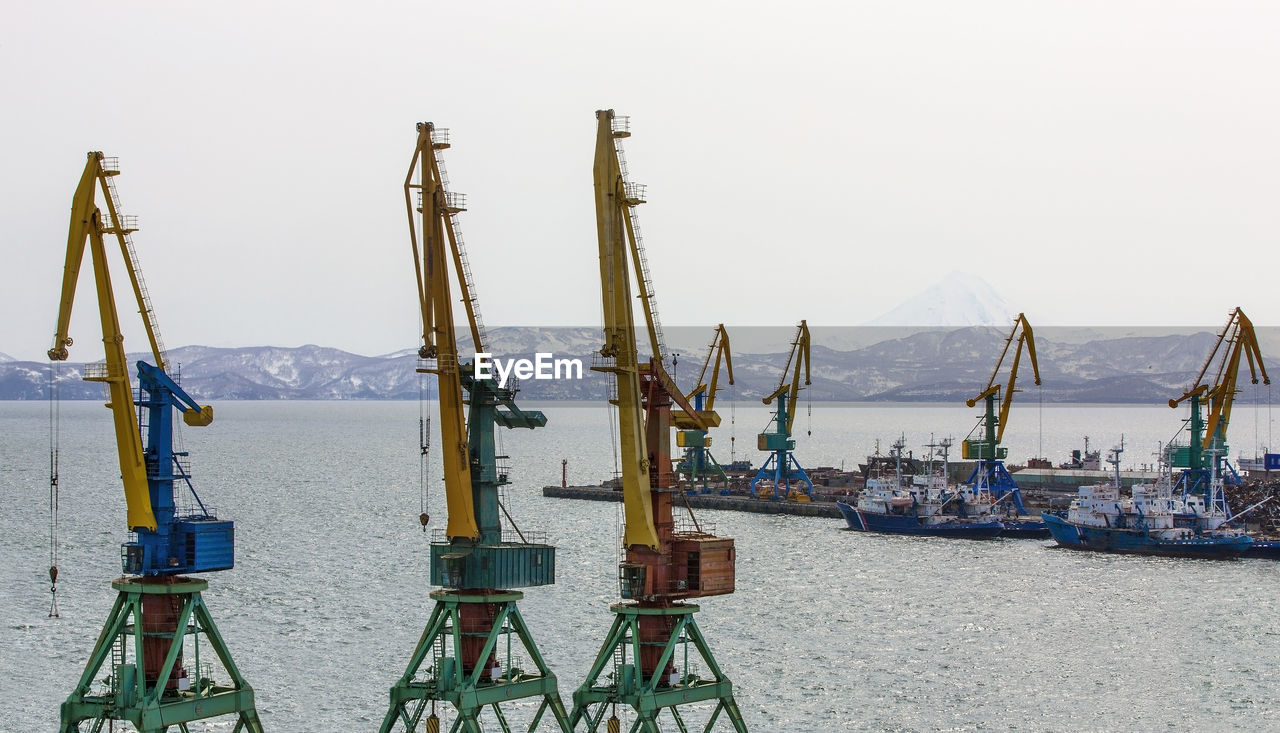 View on trading seaport with cranes, cargoes and the ship in front of snowy mountains