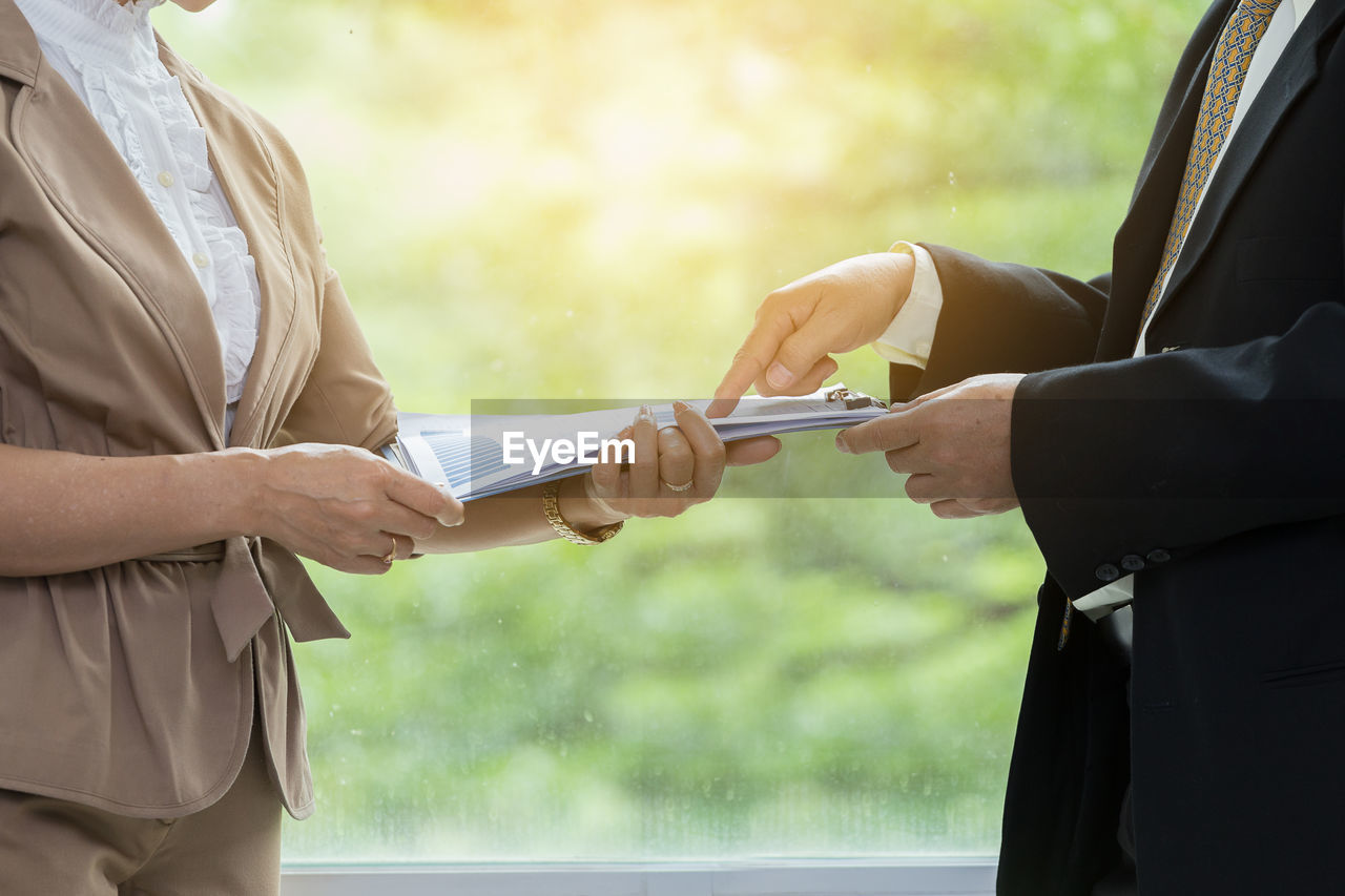 Midsection of colleague handing documents to businesswoman