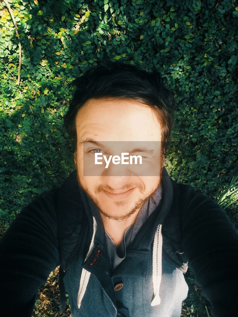 High angle portrait of man taking selfie while blinking against plants